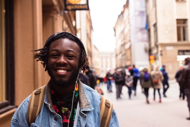 Smiling international student walking on a street while listening music